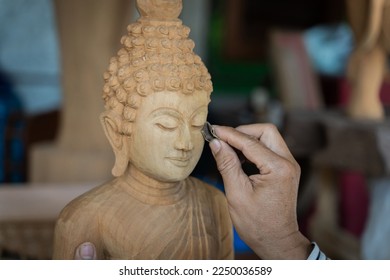 Carpenter's hands Man professional during working with woodcarving instruments Buddha statue carved from teak wood for decoration in home or modern office building. Asian craft Thai style.