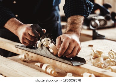 Carpenter's hands planing a plank of wood with a hand plane