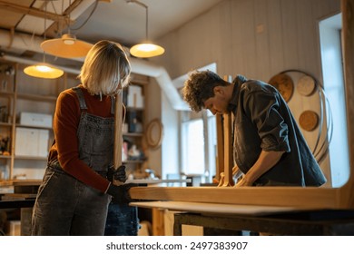 Carpentry workshop. Focused spouses woman man working in carpentry workshop assembling table, joining base and legs. Working together on an individual order. Furniture manufacturing, small business - Powered by Shutterstock