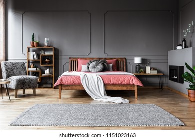 Carpet in spacious grey and pink bedroom interior with wooden bed and patterned armchair