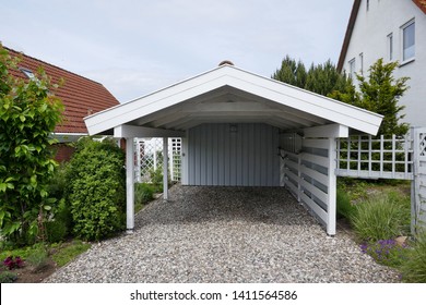 Carport with pitched roof, white wood with opeln driveway on pebble floor next to a house. Germany, Europe

