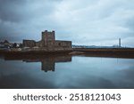 Carrickfergus Castle with a vintage effect, reflected symmetrically in calm waters. The cloudy sky and muted tones give the scene a film like atmosphere