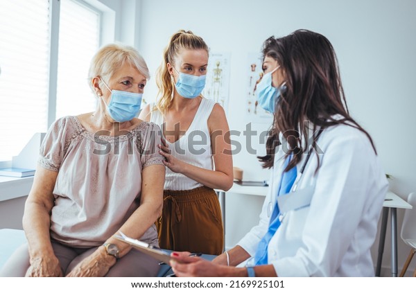 Carring  woman talks with her mom\'s\
healthcare nurse. The daughter has her arm around her mom. The\
senior woman is shaking the nurse\'s hand. Daughter sitting with\
mother at her check up\
appointment