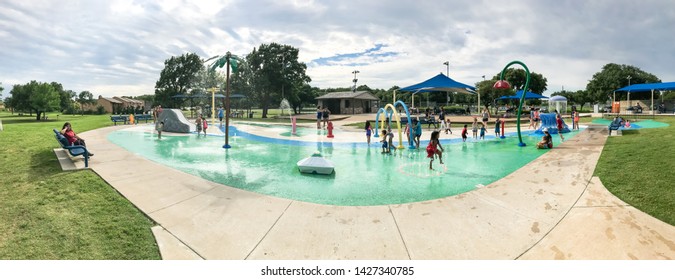 CARROLLTON, TX, US-JUNE 4, 2019: Panorama Diverse Kids Enjoy Water Splash Pad Or Spray Ground At Public Park Near Dallas. Water Fountain Activities For Children And Parent During Summer Time, Overcast