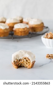 A Carrot Cake Muffin Topped With Cream Cheese Frosting With A Bite Out.