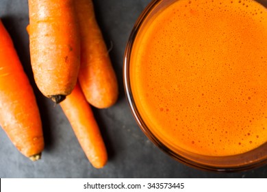 Carrot juice and carrots on a dark stone cutting board