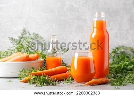 Carrot juice in a glass and bottle and fresh carrots with leaves