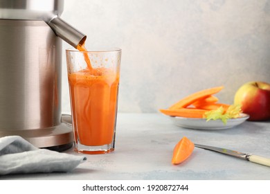 Carrot juice is poured from an electric juicer into a glass beaker.Delicious drink rich in vitamins and carotene.