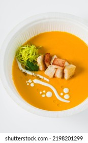 Carrot Puree Soup With Croutons And Leeks In A Plastic Takeout Container