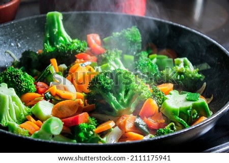 Carrots and broccoli in a hot pan while frying and steam rising.