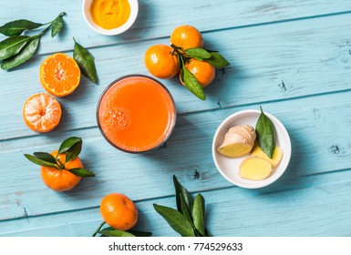 Carrots, ginger, tangerines, turmeric detox fresh juice on blue wooden background, top view. Healthy vegetarian food concept