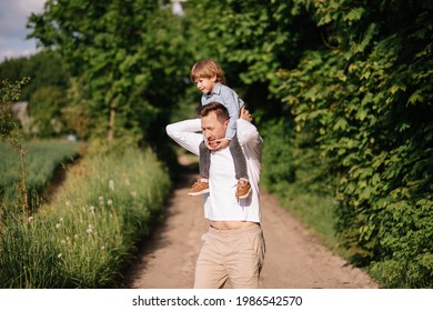 Carrying On Shoulders, Dad Along Road Among Forest And Field, Concept Of Modern Fatherhood