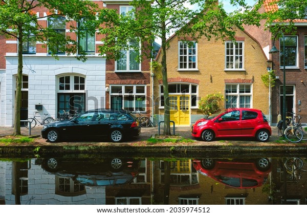 Cars and bicycles on canal\
embankment in street of Delft with reflection. Delft,\
Netherlands