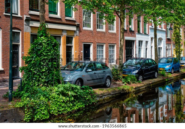 Cars and bicycles parked\
along the canal in street of Delft with reflection. Delft,\
Netherlands