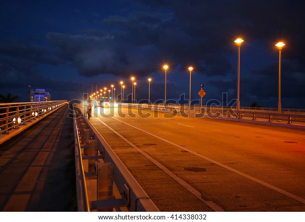 Cars and a bike\
rider travel at twilight on the 17th Street Causeway Bridge in Fort\
Lauderdale, Florida.  
