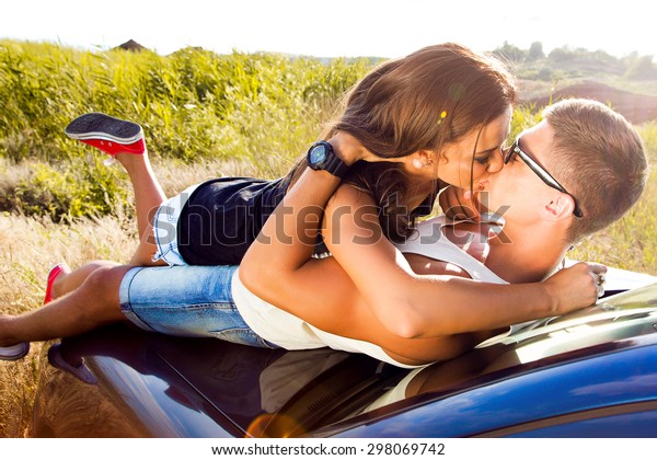 Cars - couple driving in new car smiling happy\
looking at camera and  kissing.Young people on road trip drive in\
car.Outdoor sensual couple laying on the car enjoy their trip\
together,casual outfit