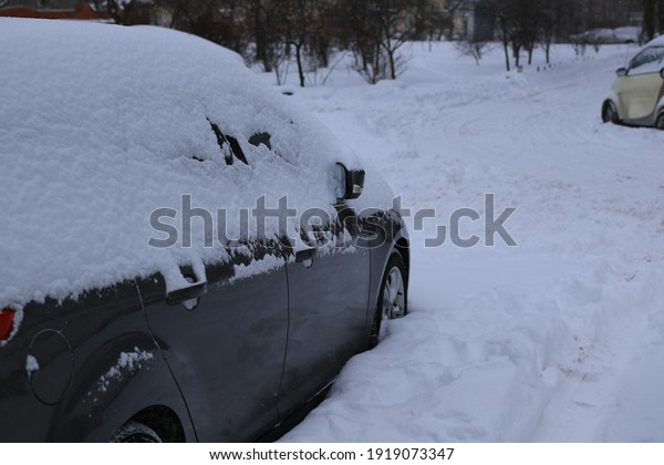 Cars covered with snow\
during snowfall in city. There is snow on the roofs, windows and\
hoods of cars. Cars in the snow-covered parking lot. Cold snowy\
winter weather.