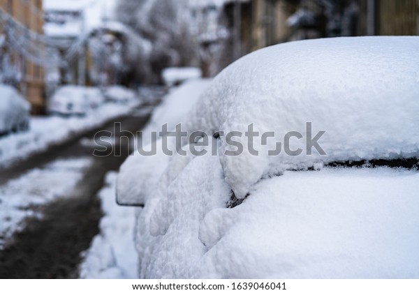 Cars covered with snow from the first snow fall of\
the year. Winter concept, snowy cars parked on the street, deep\
layer of snow