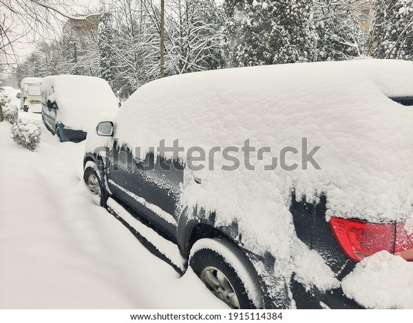 Cars covered with snow from the first snow fall of\
the year. Winter concept, snowy cars parked on the street, deep\
layer of snow