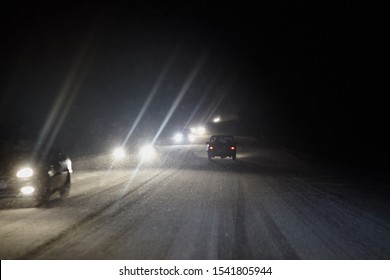 Cars Drive On The Highway In Heavy Snowfall At Black Night. Shining Headlights In The Dark. Driving In The Dangerous Conditions Of The North