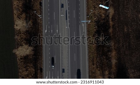 Cars driving along highway on autumn sunny day. View of cars driving on paved road. Top view. Automobile road with white markings between agricultural fields. Aerial drone view.Automobile vehicles.