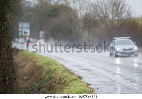 cars driving along water logged\
road with spray and rain and camera and 50 mph speed warning\
sign