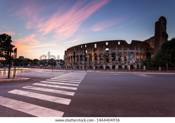 Cars fly past the world famous Colosseum in Italy\
at sunset.