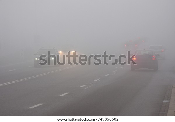 Cars in the fog.\
Bad winter weather and dangerous automobile traffic on the road.\
Light vehicles in foggy\
day.