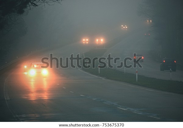 Cars in the fog. Bad\
winter weather and dangerous automobile traffic on the road. Light\
vehicles in fog.