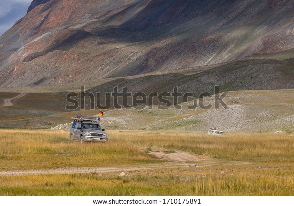 Cars with German and Mongolian flags on road\
in the desert mountain of the\
Mongolia