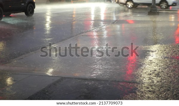 Cars lights reflection on road in rainy weather.\
Rain drops on wet asphalt of city street in USA, raindrops falling\
on sidewalk. Puddle of water on pavement. Torrential downpour or\
rainfall at night.