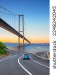 Cars in motion in the highway landscape under the Bosphorus bridge. Road landscape at colorful sunset. Car driving on the road. Nature scenery on city beach. Travel journey for summer trip on road.