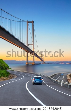 Cars in motion in the highway landscape under the Bosphorus bridge. Road landscape at colorful sunset. Car driving on the road. Nature scenery on city beach. Travel journey for summer trip on road.