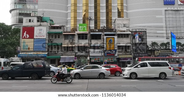 Cars and motorbike line up for traffic lights on\
Asoke road with shophouse building in the background. Bangkok,\
Thailand 12th July 2018
