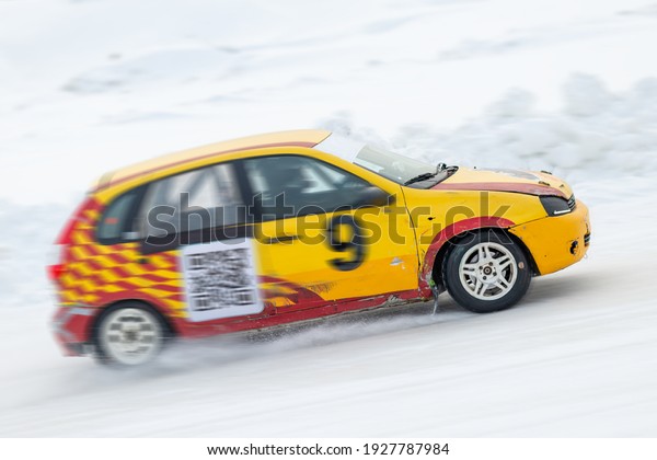 Cars on the autocross. Racing in the open air on\
snow. The racing car (in soft focus) is racing on the fast track\
with the blur motion effect. Sliding. It\'s snowing, a snowy road in\
winter.