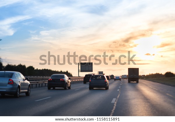 Cars on busy road driving in evening\
sunset. highway with metal safety rail or\
barrier.