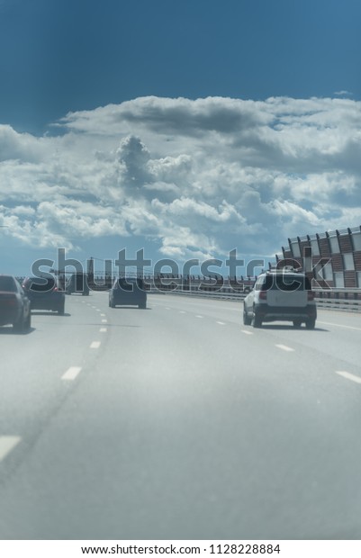 A lot of cars on the road. Noise\
barrier on highway in the city. Blue sky and white\
clouds