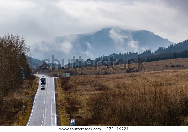 Cars on a winding mountain road in a small village.\
The tops of high mountains are hidden by clouds. Fog. Autumn\
landscape. Panoramic view.