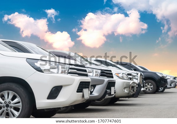 Cars park in\
asphalt parking lot in a row with cloudy sky background in nature.\
Outdoor parking lot with fresh ozone, green environment of\
transportation and technology\
concept\
