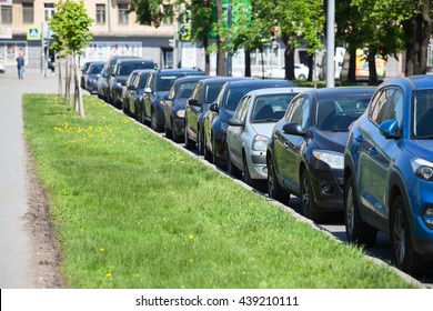 Cars Parked In Line On The Roadside. Green Grass In City Street