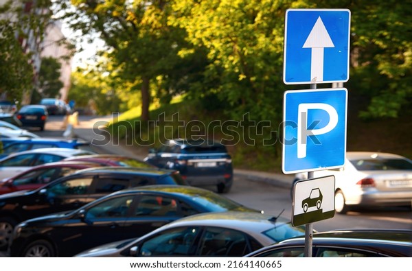 Cars parked on parking\
lot at downtown, parking problems not enough free space. Crowded\
public parking lot on narrow street. Rows of cars parked on\
roadside, parking sign. 
