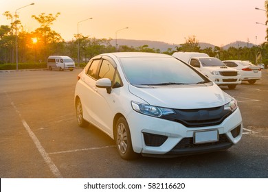 Cars parked in outdoor parking lot at a park in the evening time with  sunlight of sunset and beautiful orange sky background