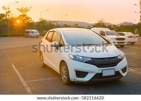 Cars parked in outdoor parking lot at a park in the evening time with  sunlight of sunset and beautiful orange sky background