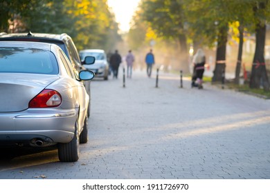 Cars Parked In A Row On A City Street Side On Bright Autumn Day With Blurred People Walking On Pedestrian Zone.