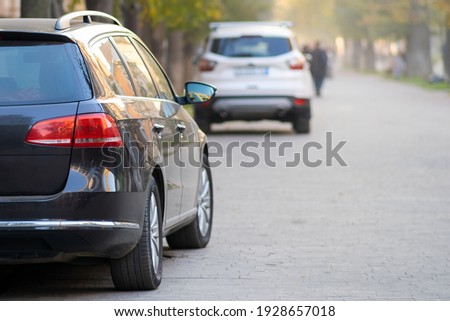 Cars parked in a row on a city street side on bright autumn day with blurred people walking on pedestrian zone.