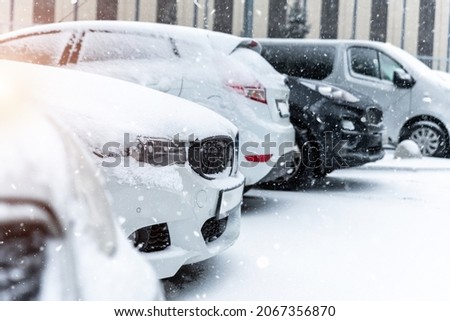 Cars parked in row at outdoor parking in winter. Vehicles covered by snow during heavy snowfall. Snowstorm or blizzard cold season weather forecast. Ice storm automobile park lot storage at morning