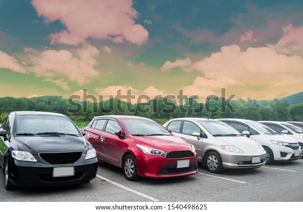 Cars parking in asphalt parking lot in a row\
with trees, colorful cloudy sky background in a park. Outdoor\
parking lot with fresh ozone, green environment of transportation\
and technology concept\
