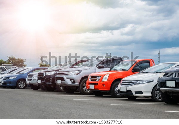 Cars parking\
in asphalt parking lot in a rows with cloudy sky background in a\
park. Outdoor parking lot with fresh ozone, green environment of\
transportation and technology\
concept\
