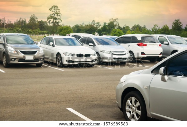 Cars parking in\
asphalt parking lot with trees, cloudy sky background in a park.\
Outdoor parking lot with fresh ozone, green environment of\
transportation and technology\
concept\
