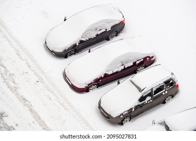 Cars in the parking lot covered with snow. Automobiles snowdrifts by the road in the yard of the house. Aerial top view. The concept of a bad winter morning.